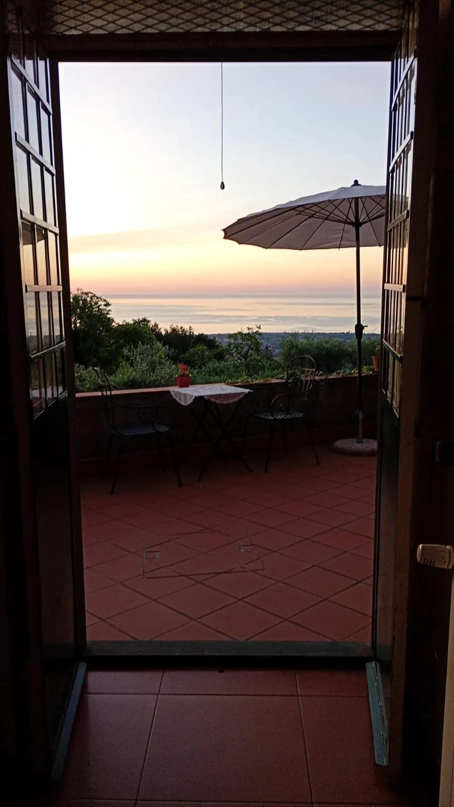 Shuttered doors opening onto a terracotta terrace above the Sicilian coast at dusk